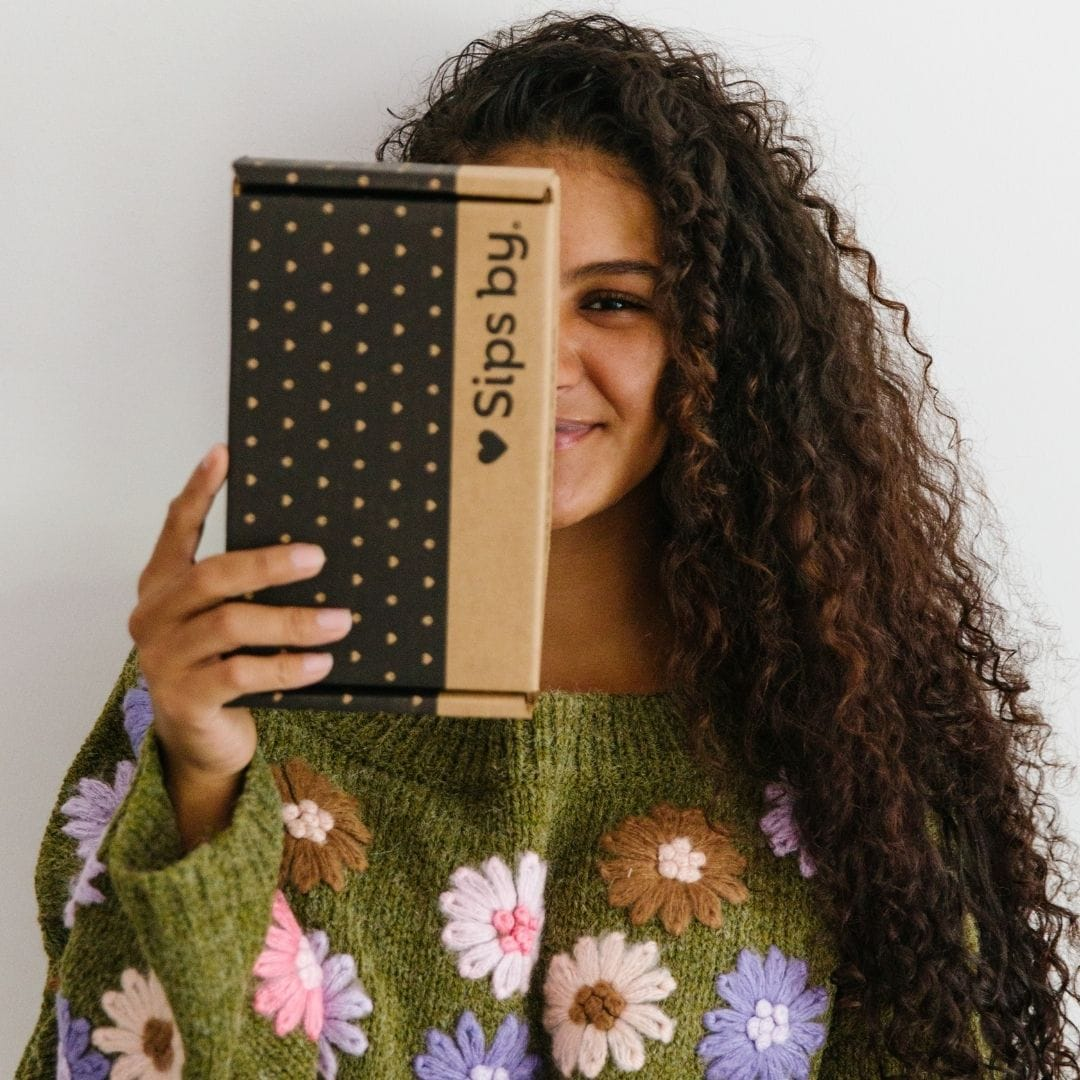 Woman wearing a green floral sweater and holding a Sips by Box and smiling