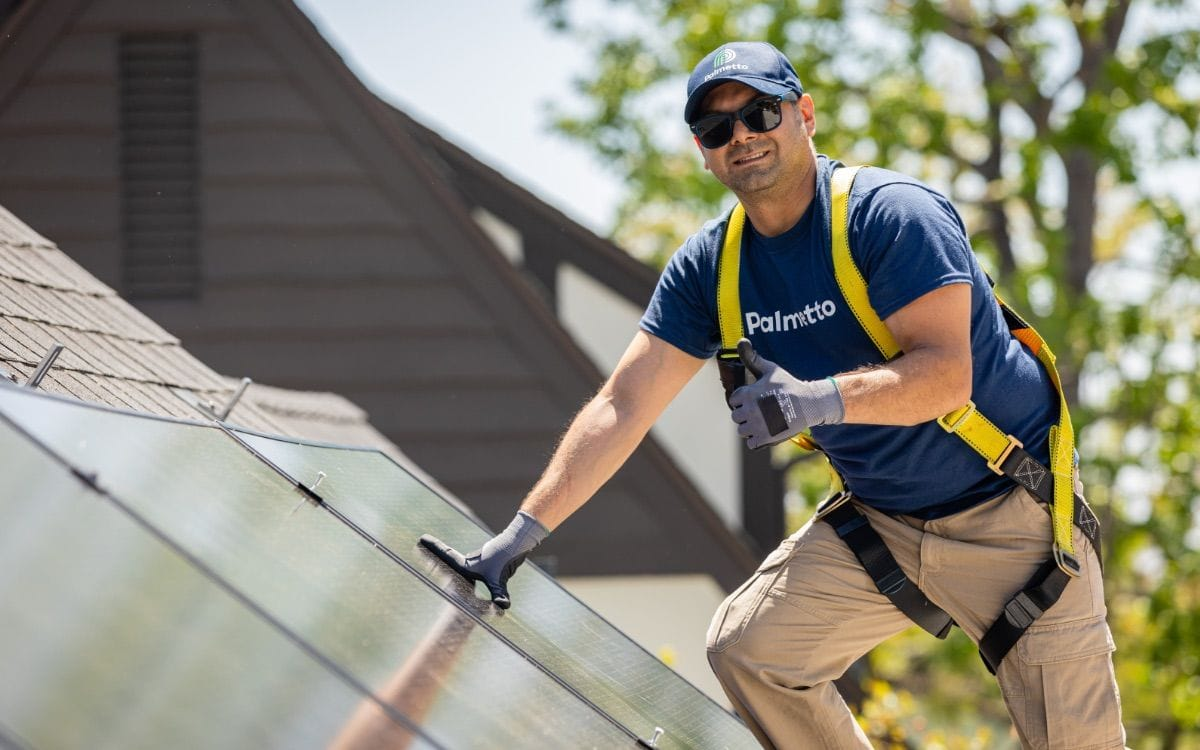 A Palmetto solar installer, giving the thumbs up next to a solar panel assembled in the USA.