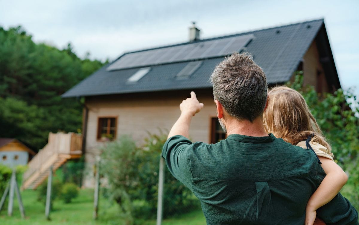 Man holding a child in his arms and pointing to a solar-powered roof