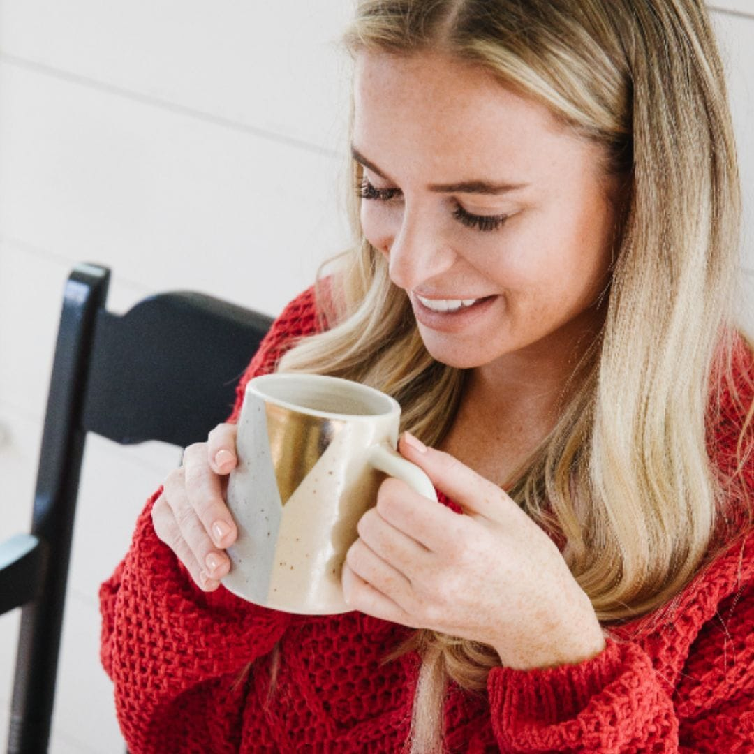 Woman in a red sweater holding a mug of tea, sitting on a black bench, and smiling