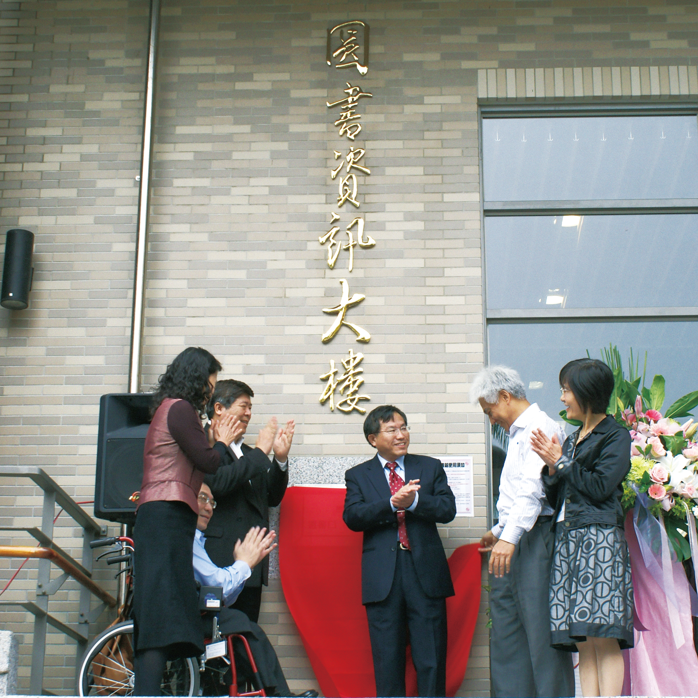 許多人於圖書館招牌前微笑鼓掌