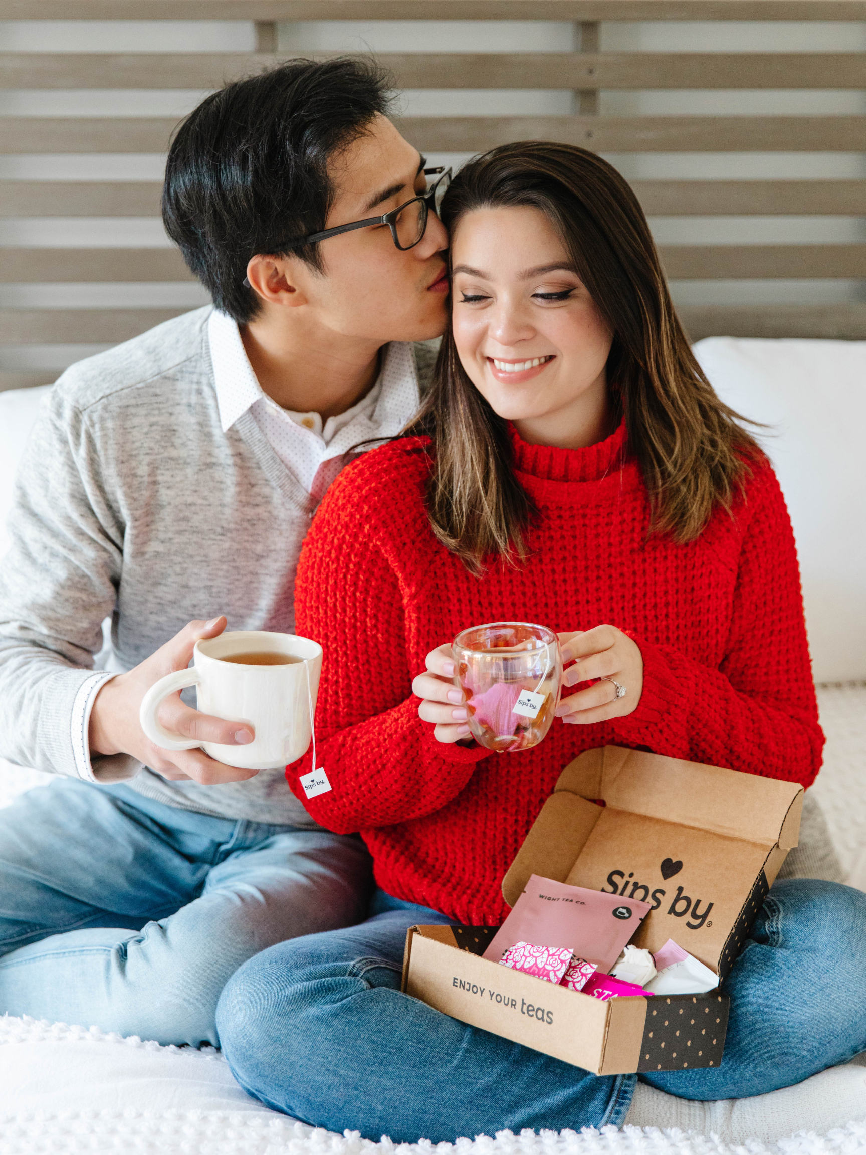 A couple in gray and red sweaters holding cups of tea and a Sips by Box