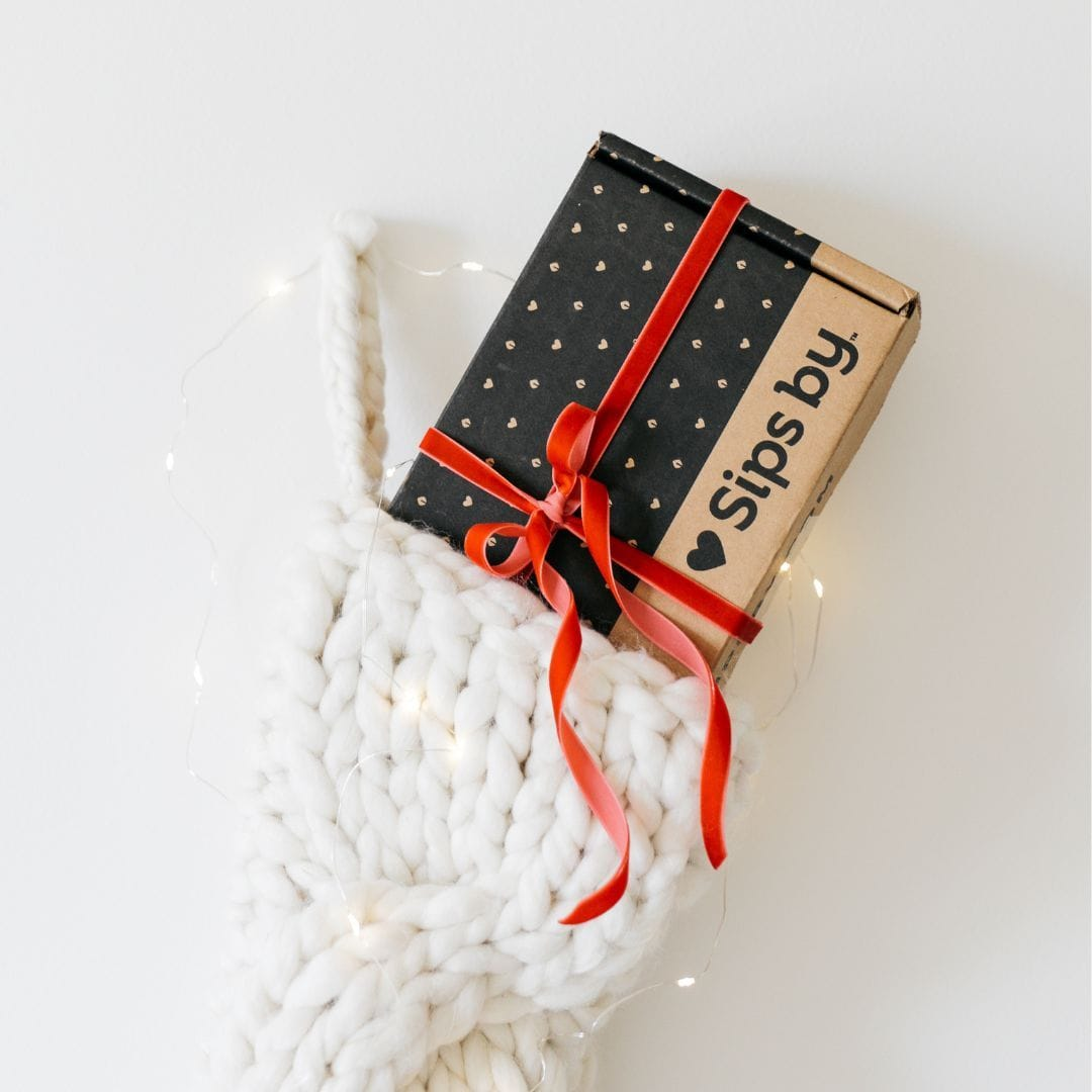 White stocking with a Sips by Box sticking out wrapped in a red bow