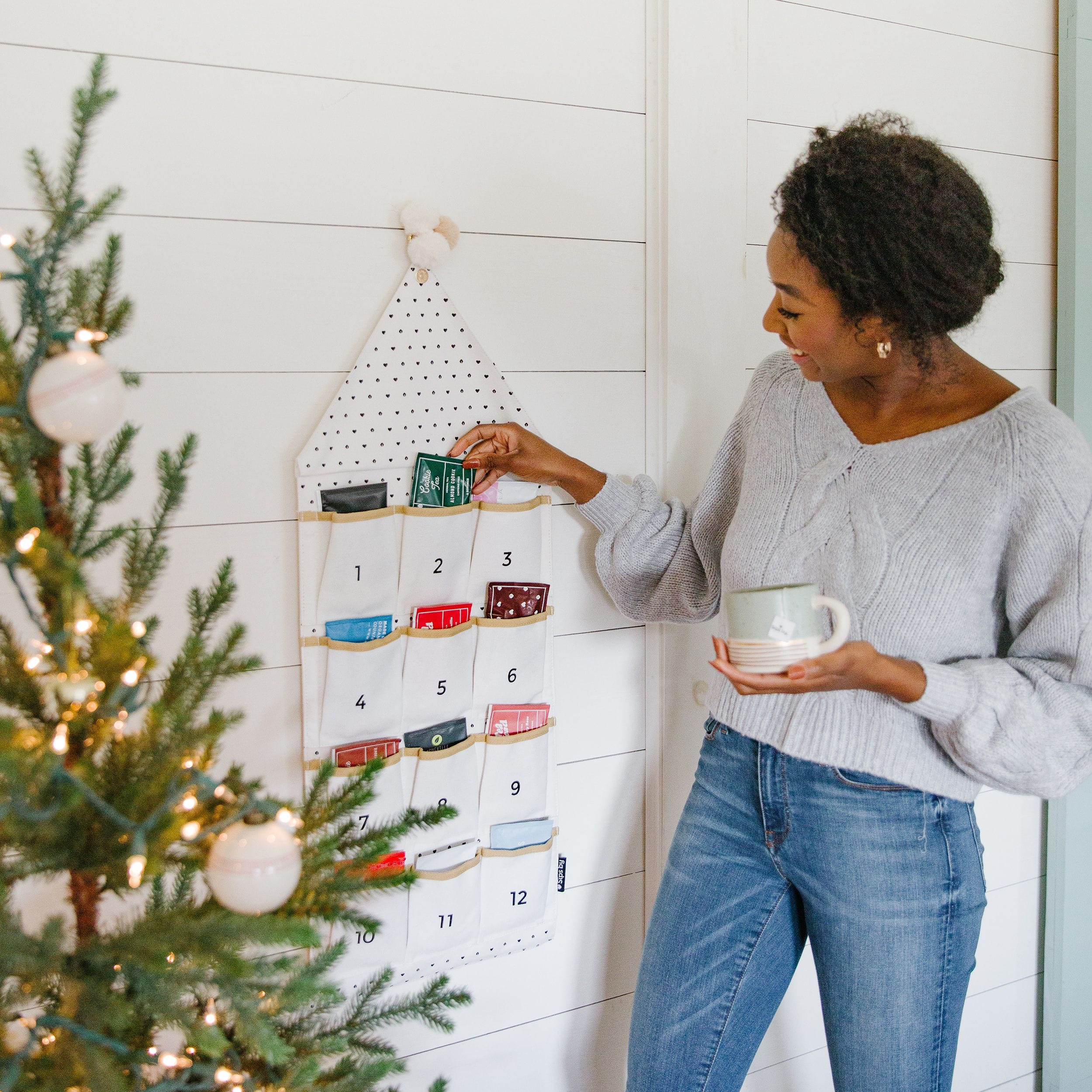 Woman choosing a tea from Sips by's Holiday Tea Advent Calendar hanging on a wall