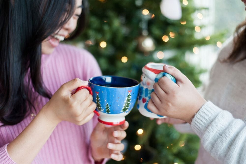 Green sweater wrapped sleeves holding up a white and gold Santa mug with Sips by tea