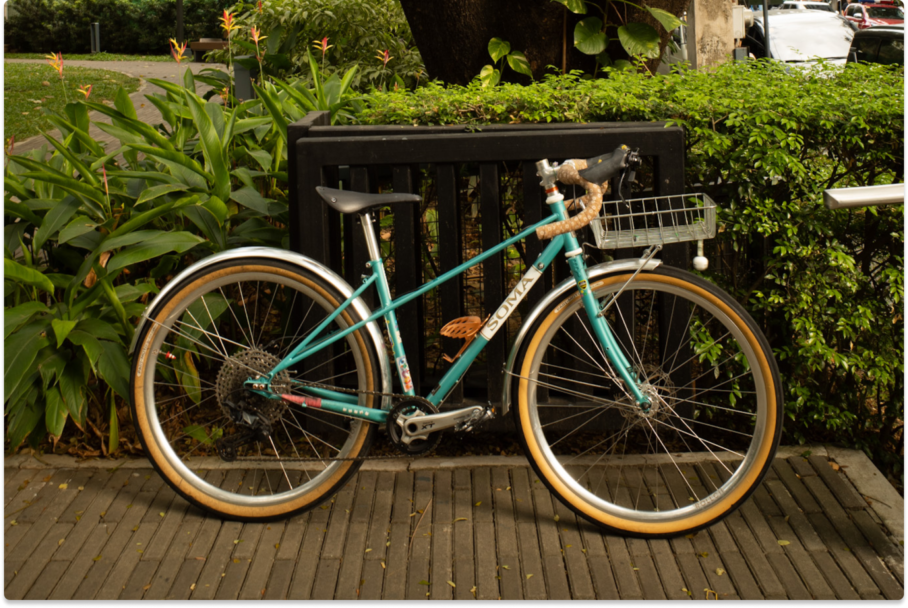 A profile of a teal-colored bike against a black gate and greenery.