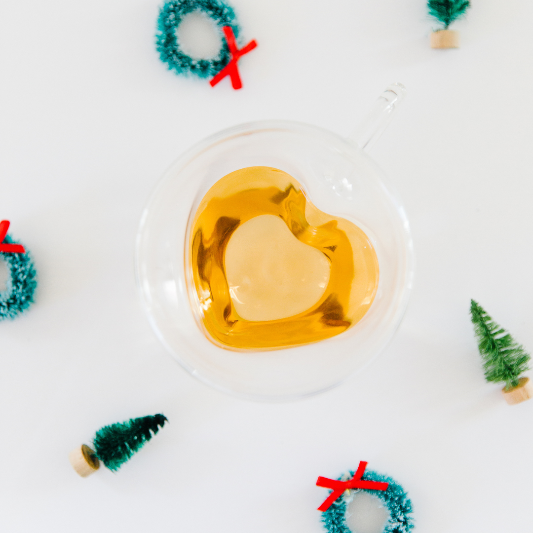 Wellness tea gifts photo of a cup of tea in a glass heart mug surrounded by mini Christmas trees and wreaths decor