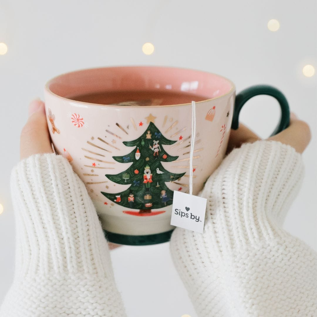 Hands holding a tea mug with a Christmas tree