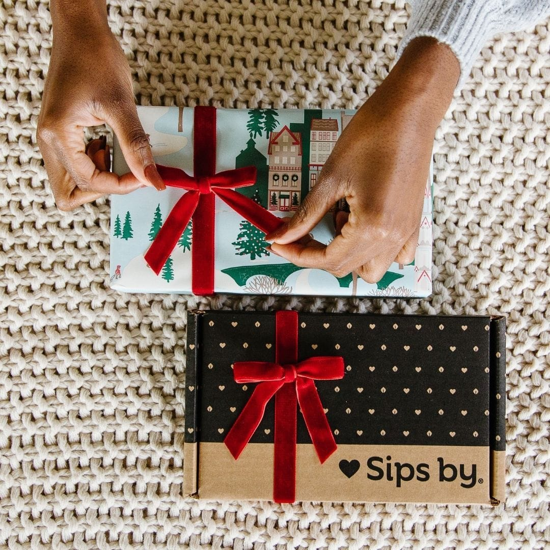Hands tying a red bow on a wrapped Sips by Box