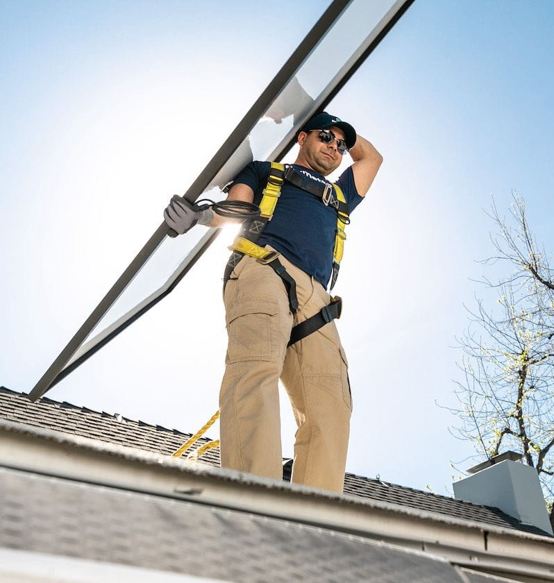 Palmetto solar installer holds panel on his shoulder during a sunny installation