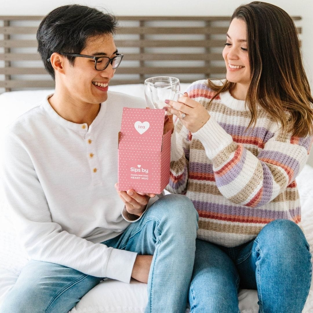 Smiling couple opening a glass tea heart mug gift