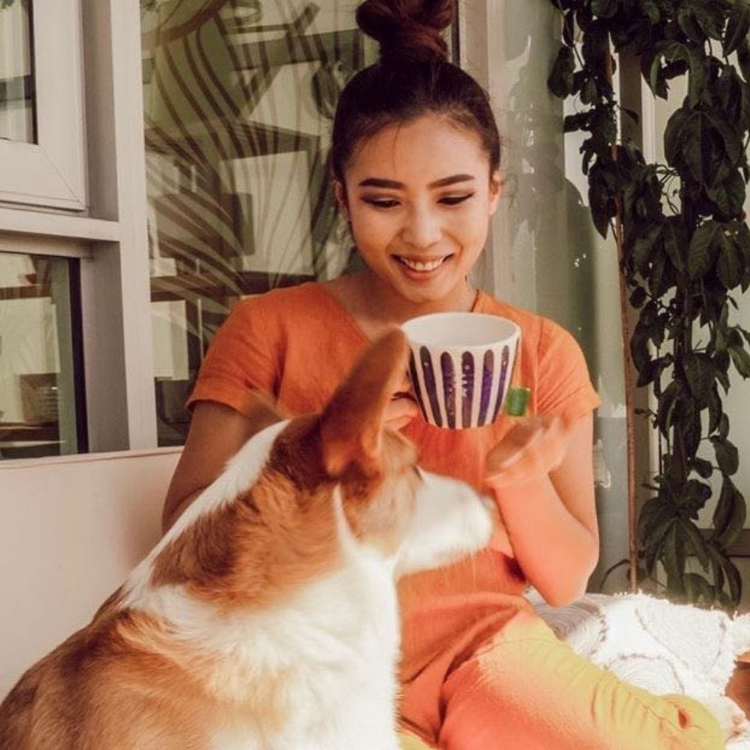 Smiling woman in orange outfit drinking a cup of tea and looking at her dog