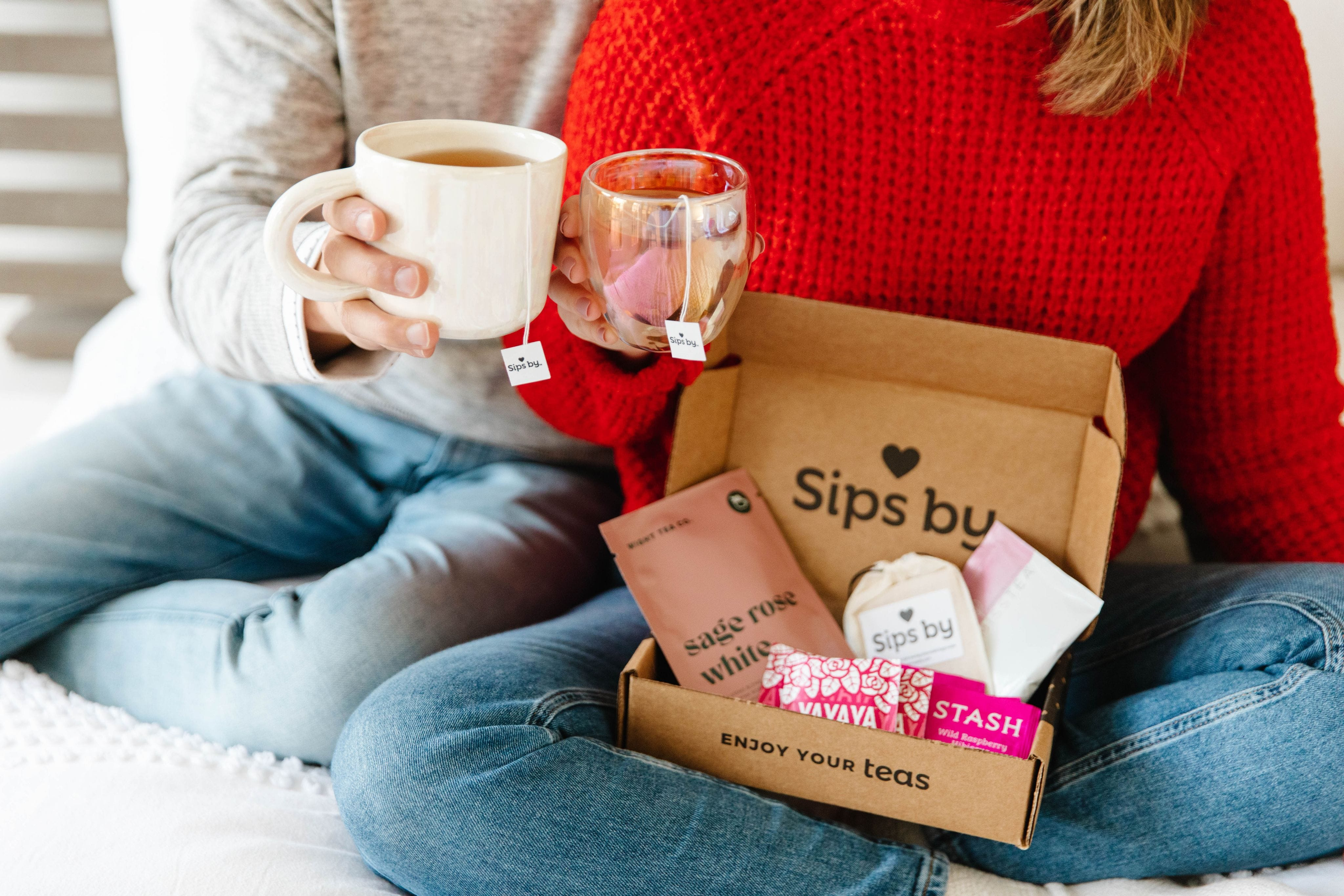 Scene of a couple cheersing their Sips by tea mugs with an open Sips by Box in one person's lap
