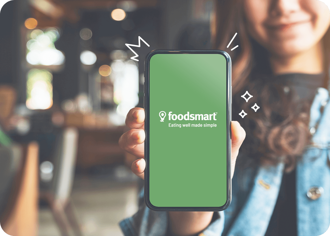 Photo of a happy customer holding a phone aloft which is opening the Foodsmart mobile app