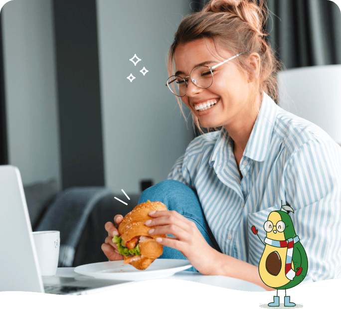 Photo of a happy woman eating a sandwich while using her computer