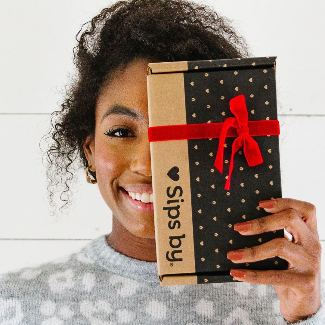 Two people in a pink and gray sweater exchanging a Sips by Box tea gift wrapped in a white bow