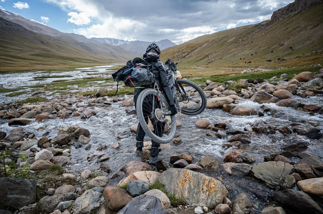 silk road mountain race cycliste porte son vélo dans rivière rocheuse