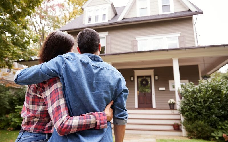 Man and woman looking up at a three-story beige house.