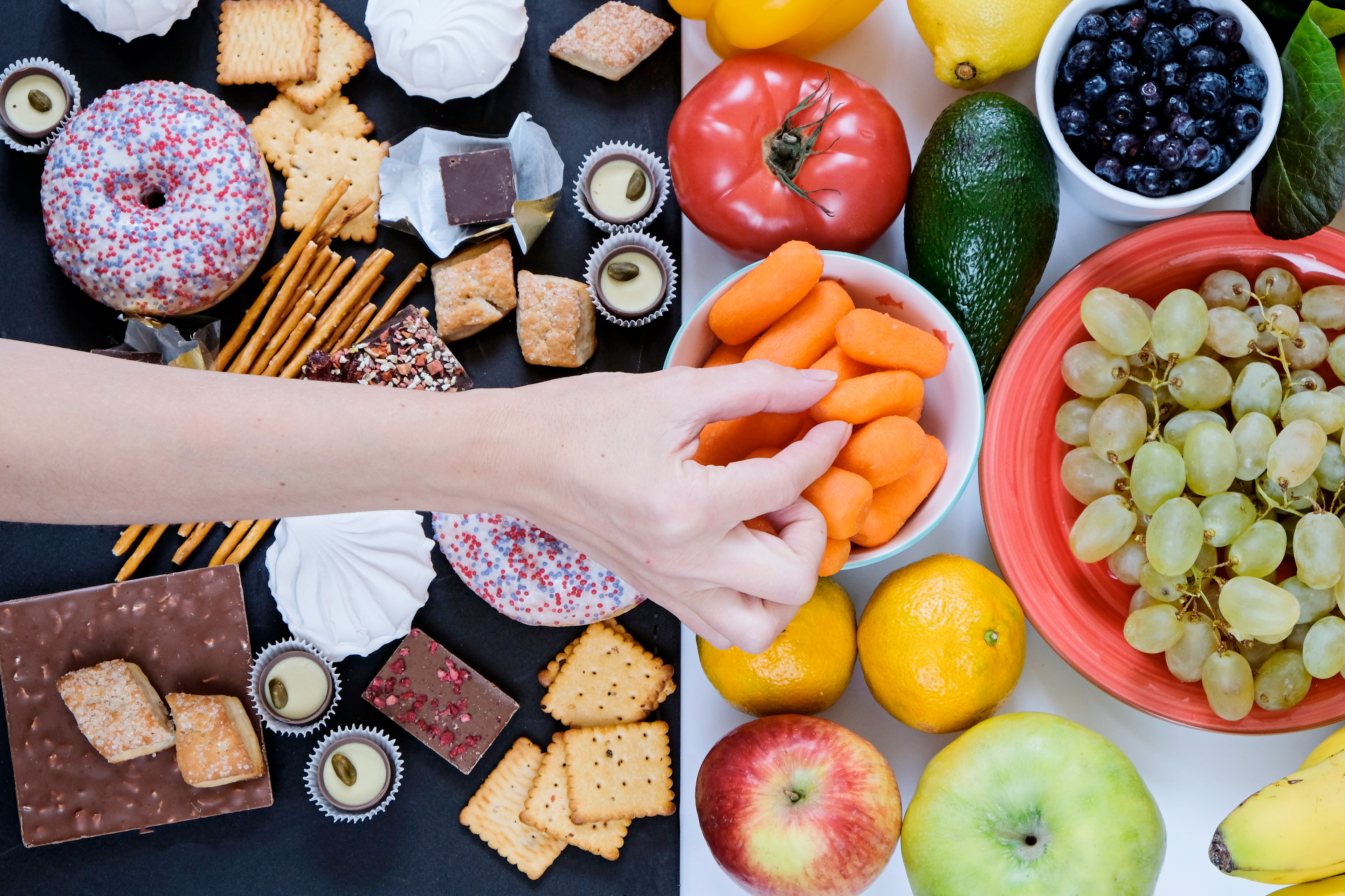 Photo of a hand reaching past junk food to grab a healthy snack