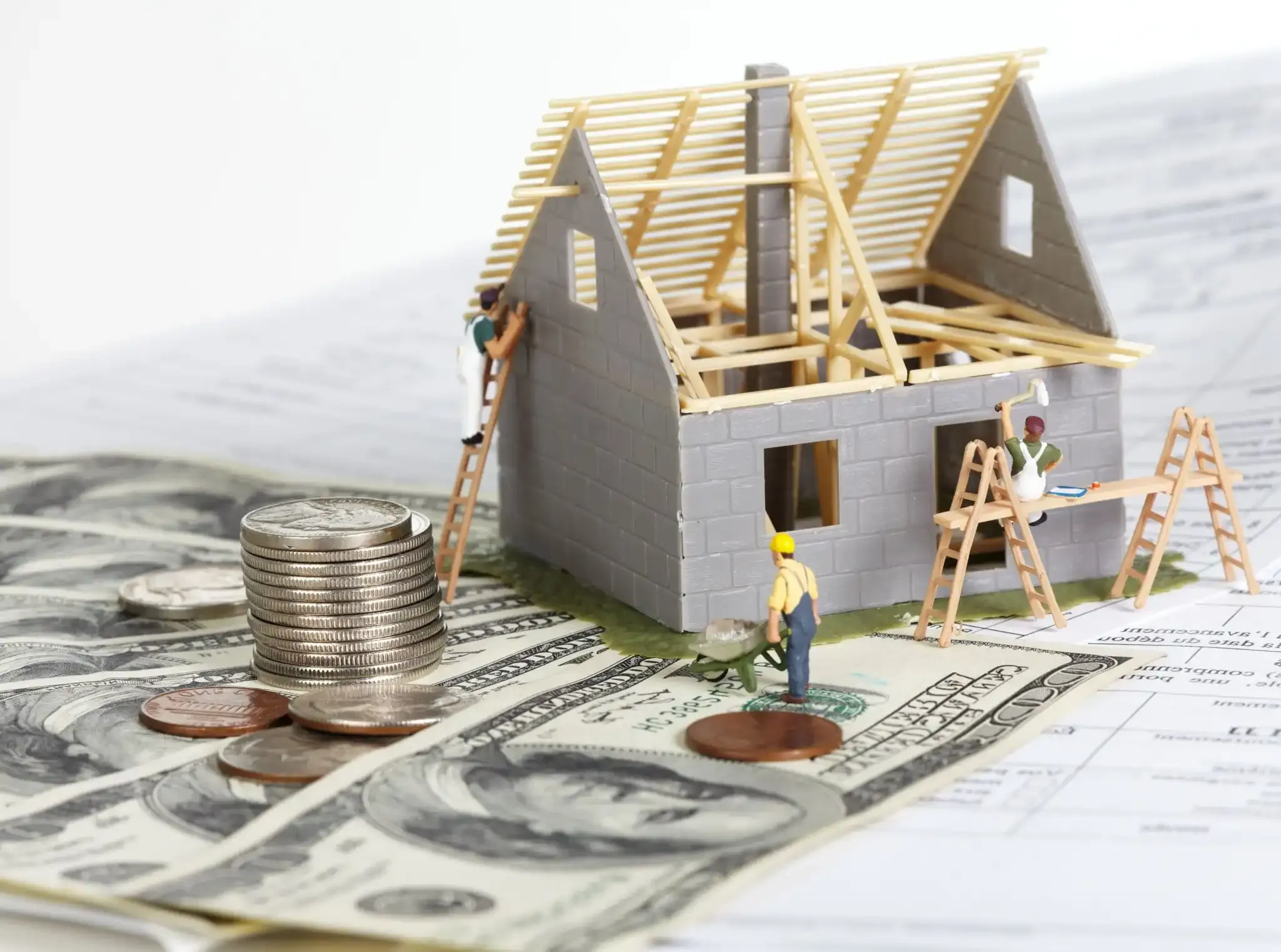 Model of house being built by construction workers near money and forms