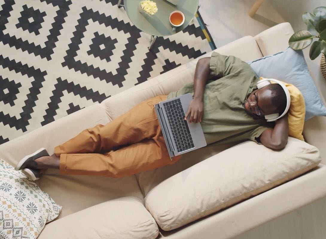 Video screenshot of a man relaxing on his couch with a laptop and headphones