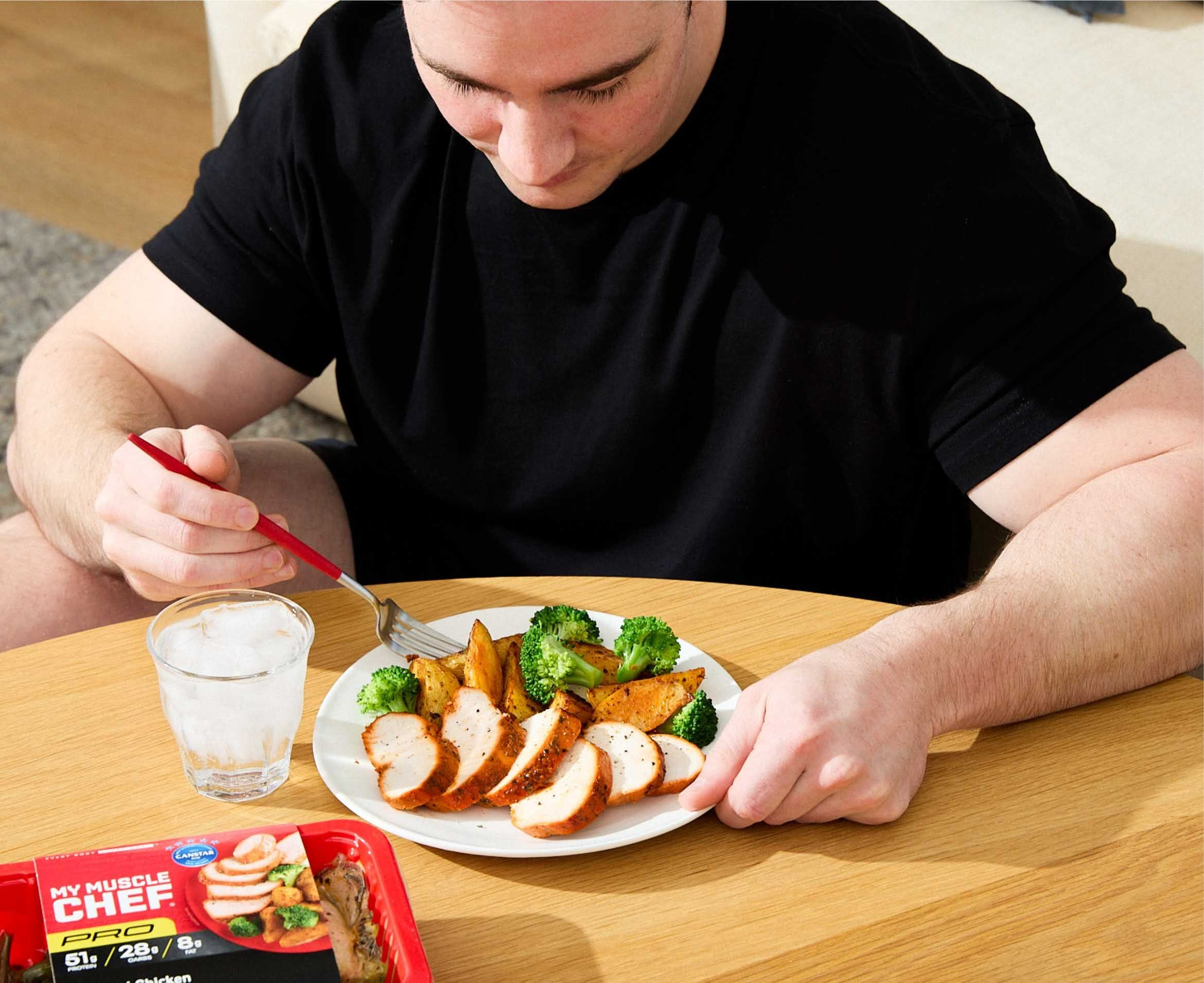 Man enjoying a healthy meal with chicken, broccoli, and sweet potatoes, alongside a My Muscle Chef meal package.