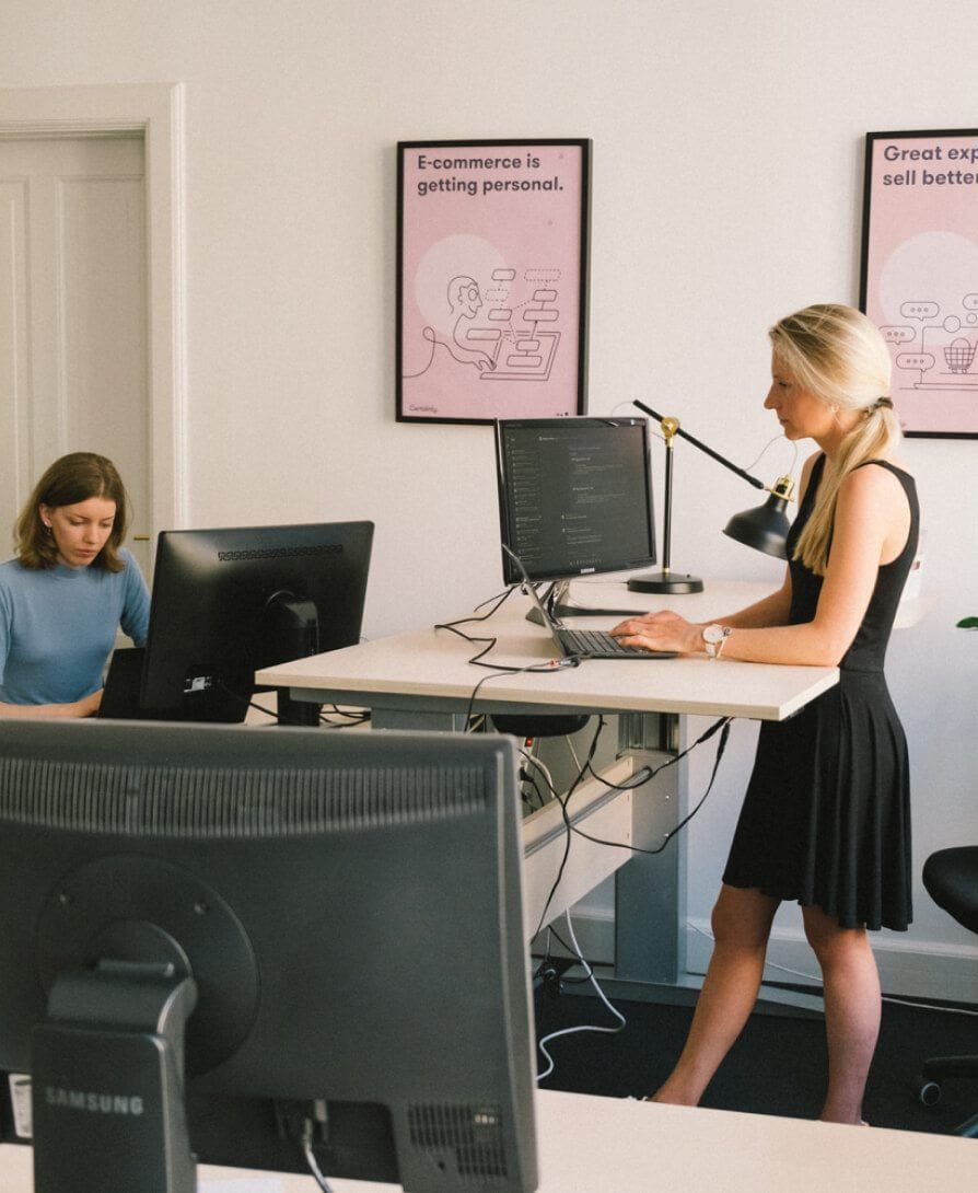 Two young women sitting at a desk in an office, focused on their screens.