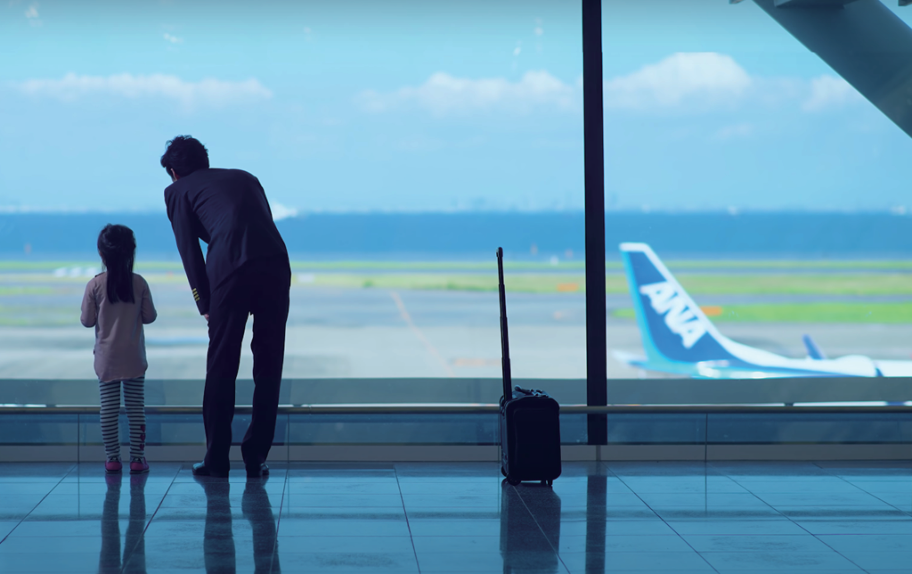 A man and a girl looking at an ANA plane through the window in the airport