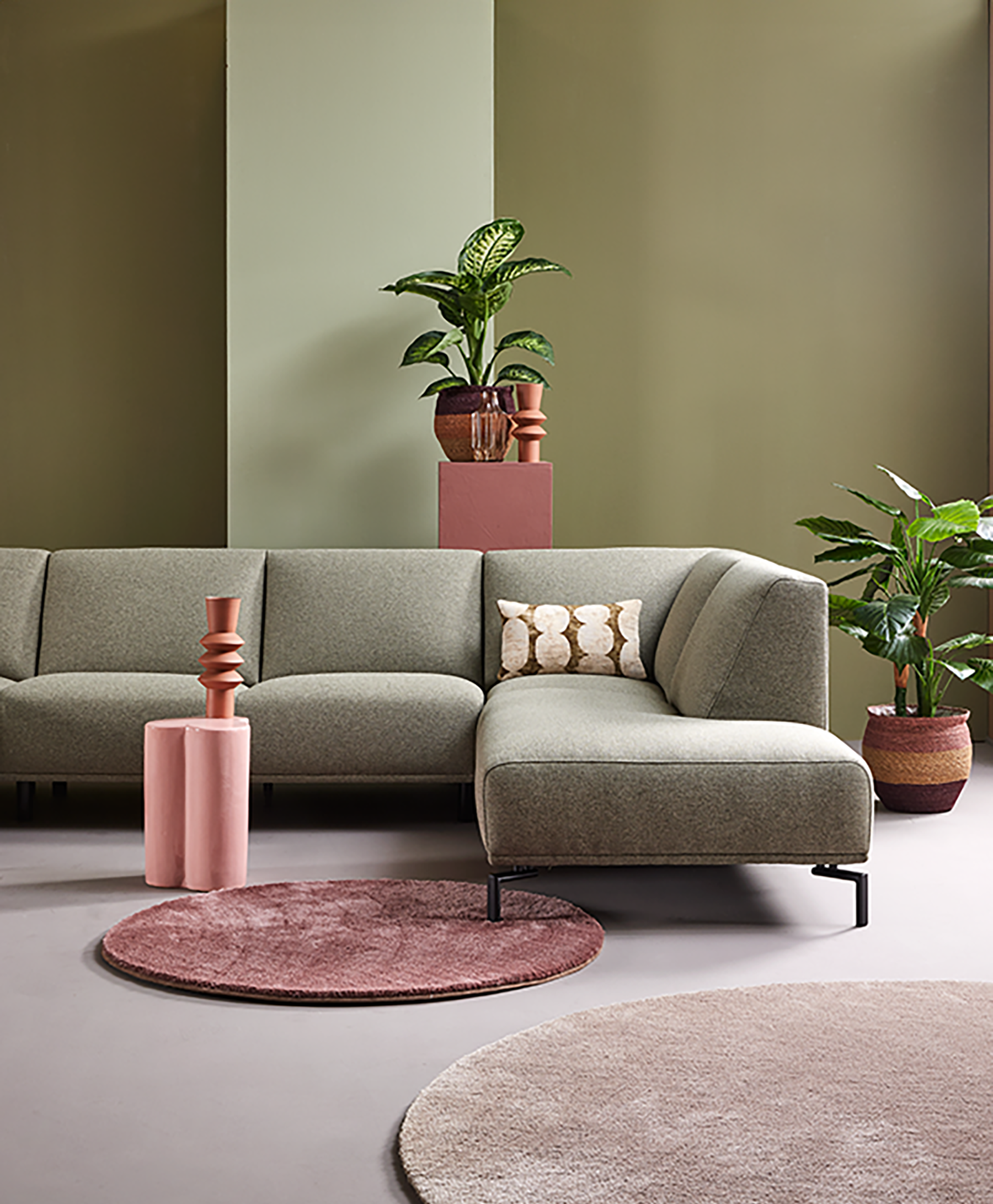 Modernes weißes Ecksofa vor farbenfroher Wand in Lila, Pink und Blau, dekoriert mit orange-weiß kariertem Kissen, Glasvase mit roten Zierblumen und rundem Teppich in Beige-Lila für stilvolles Wohnzimmerdesign.