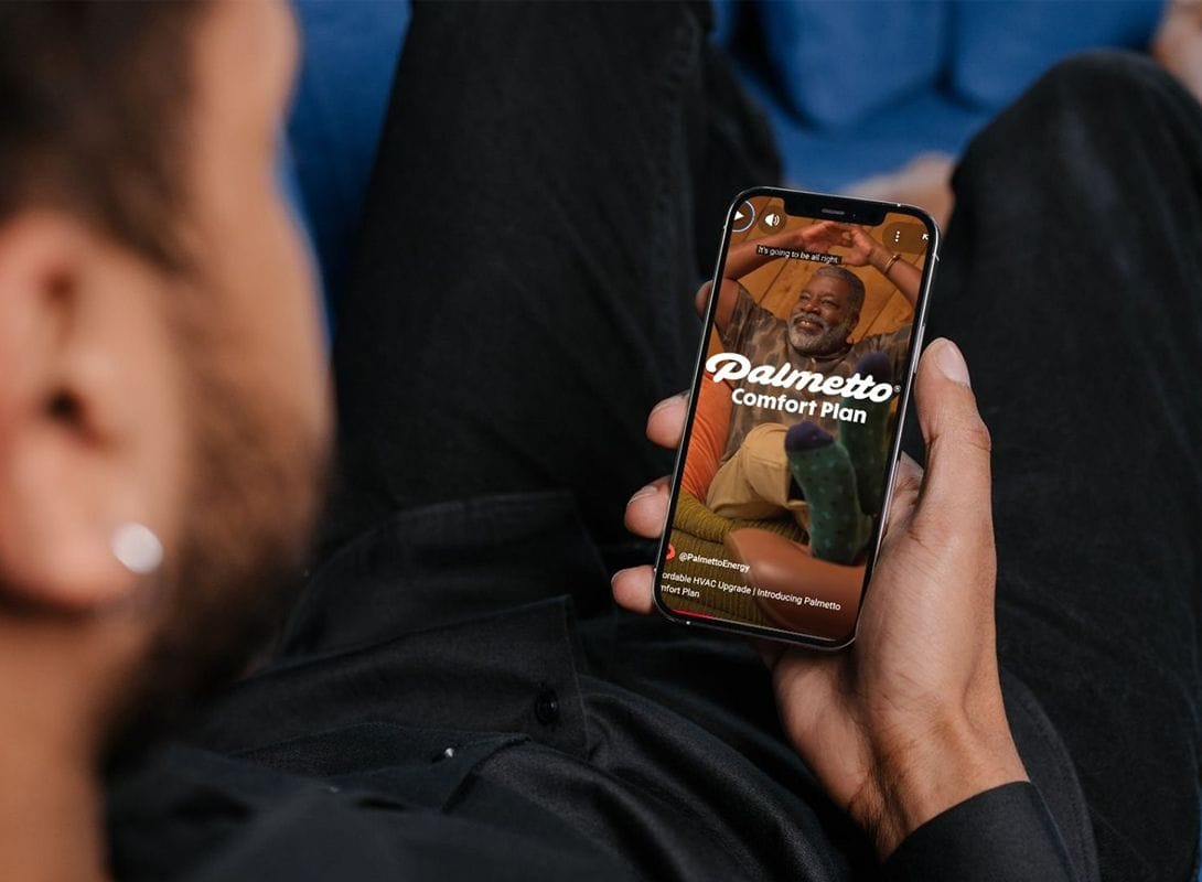 a man on the couch watching a teaser for the Palmetto Comfort Plan on his phone
