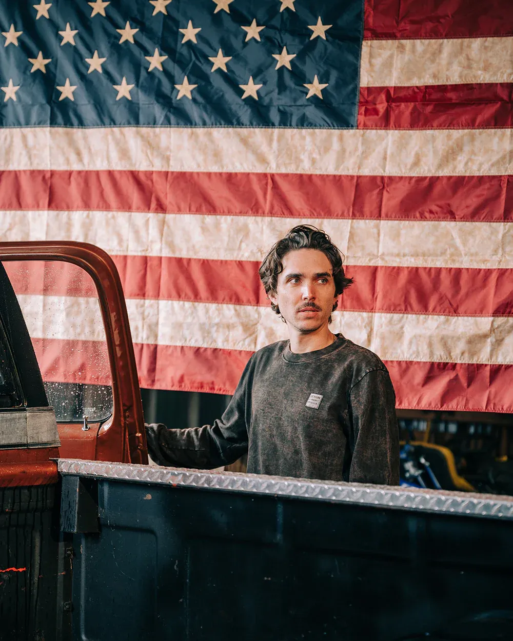 man wearing a devium long sleeve shirt in front of an american flag