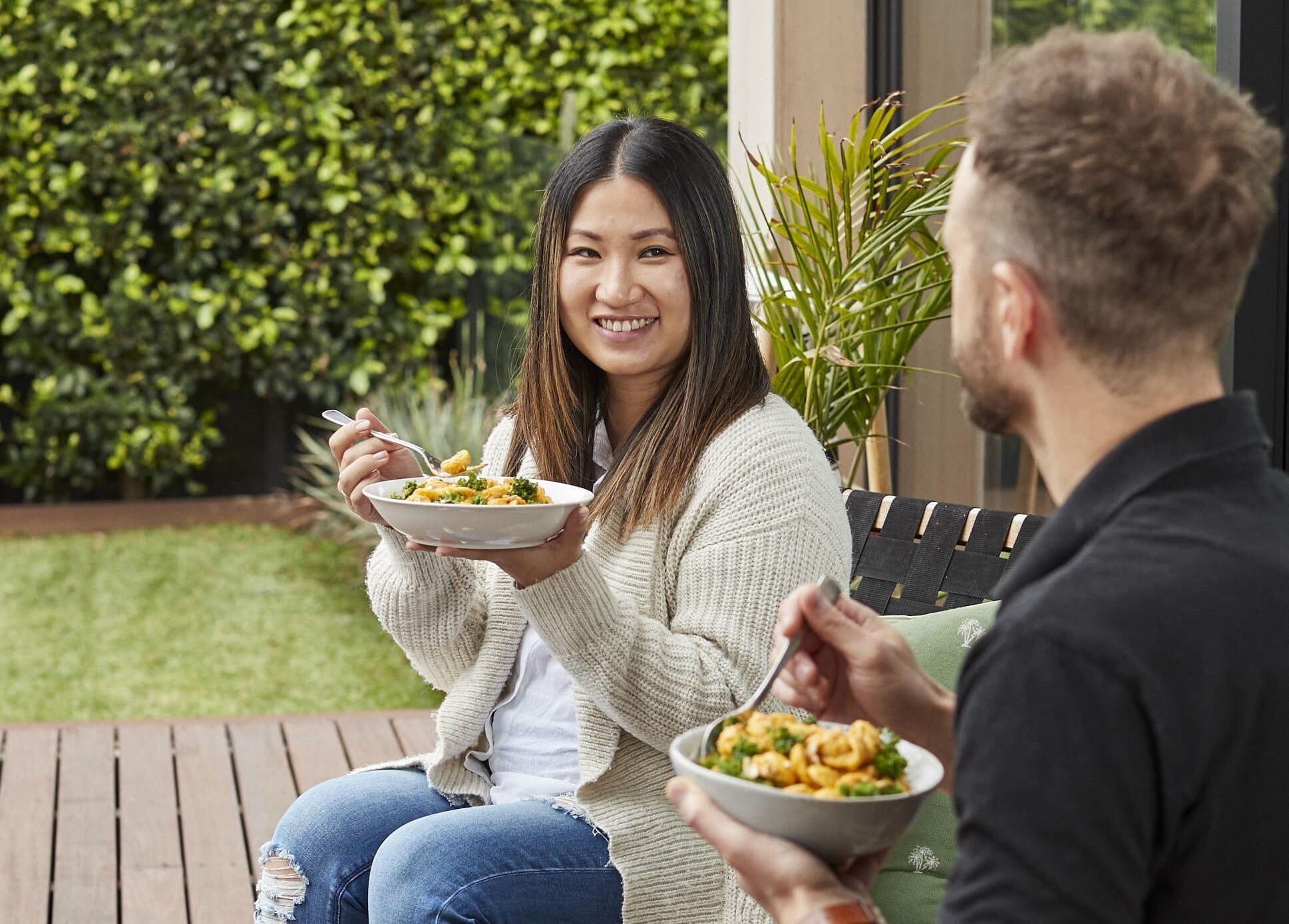 Man enjoying a healthy meal with chicken, broccoli, and sweet potatoes, alongside a My Muscle Chef meal package.