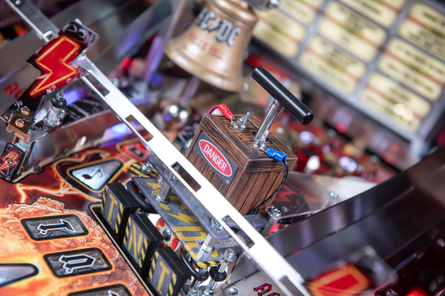 A custom sculpted denonator box with a custom sculpted bell in the background onA lower playfield with illuminated inserts on the AC/DC Remastered pinball machine by Stern Pinball.
