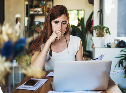 A woman looking serious at her computer with a utility bill in her hand