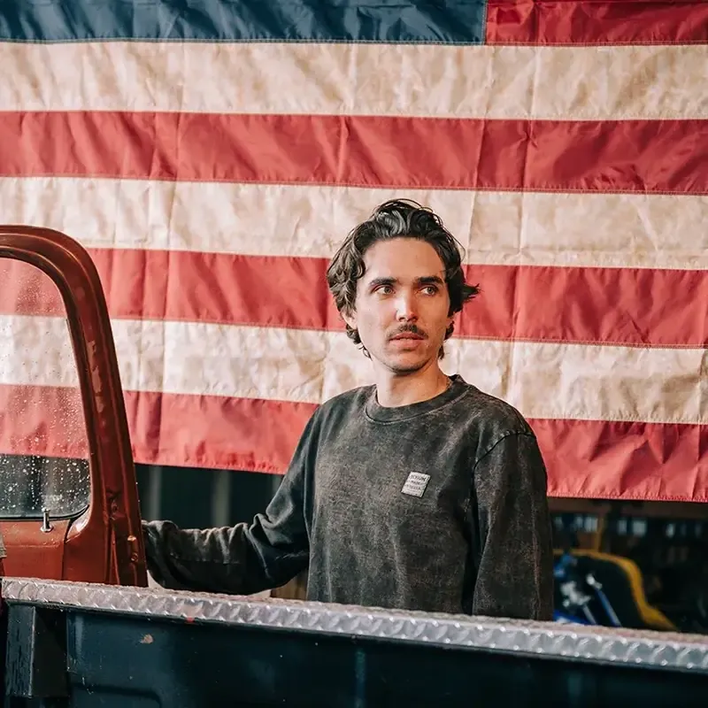 man wearing a devium long sleeve shirt in front of an american flag