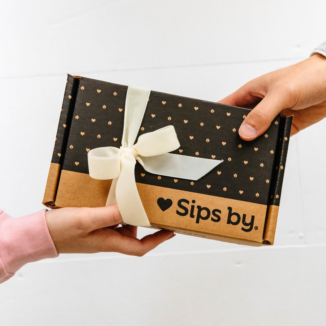 Hands tying a red bow on a wrapped Sips by Box